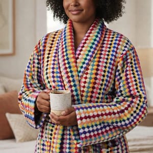 May include: A vibrant, patterned dressing gown with a shawl collar. The gown has a repeating dot pattern in multiple colours. A white speckled mug with a dark drink is held.