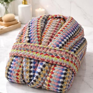 May include: A multi-coloured, patterned bathrobe with a textured, woven design. The robe features a mix of colours including blue, pink, yellow, and green. The robe is folded and appears to be made of a soft, absorbent material, ideal for after a shower or bath.