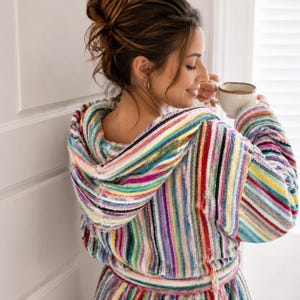 May include: A hooded bathrobe featuring a vibrant, multi-colored vertical striped pattern in shades of pink, teal, yellow, blue, and white. The garment is made of a textured, absorbent terry cloth fabric and includes a matching tie belt at the waist.