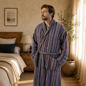 May include: A long-sleeved bathrobe featuring a multi-colored vertical striped pattern in shades of blue, purple, red, and teal. The garment includes a shawl collar, a matching fabric tie belt at the waist, and two large patch pockets on the front.