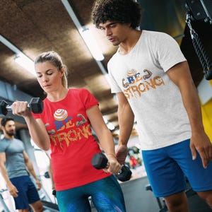 Be Strong T-Shirt - Motivierendes Gym T-Shirt mit Muskelarmen Grafik - Fitness Workout Shirt für Männer & Frauen, Bodybildungsbekleidung