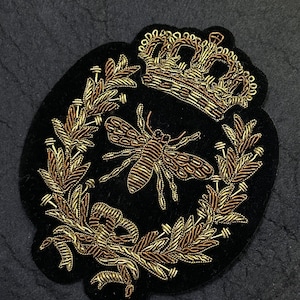 Puede incluir: Parche bordado negro con un diseño de abeja, corona dorada y corona de laurel. La abeja y la corona están detalladas con hilo dorado y marrón. El parche mide aproximadamente 7,6 cm de ancho.