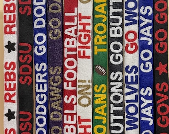 Könnte beinhalten: Eine Sammlung von Perlen-Lanyards in verschiedenen Farben, die jeweils Teamnamen und Sätze wie "REBS", "GO DODGERS" und "TROJANS" zeigen. Die Lanyards haben goldfarbene Verschlüsse und sind nebeneinander angeordnet.