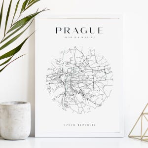 Op de afbeelding: Een ingelijste print met een gedetailleerde zwart-wit kaart van Praag, Tsjechië. De naam van de stad staat bovenaan afgedrukt, met coördinaten eronder. De woorden "Czech Republic" staan onderaan afgedrukt. De print wordt weergegeven op een wit oppervlak.