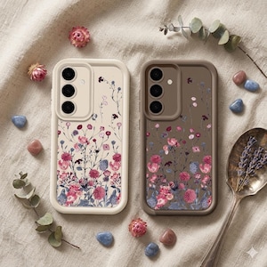 Puede incluir: Dos fundas para teléfono con diseños florales. Una es de color blanco roto con flores rosas, azules y moradas. La otra es marrón con patrones florales similares. Ambas tienen un módulo de cámara con tres lentes.