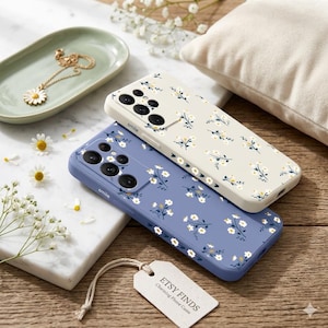 May include: Two phone cases with floral patterns. One is light blue, the other is off-white. Both cases have a daisy-like floral design with the word "smile" printed on the bottom. A tag that says "ETSY FINDS Charming Phone Cases" is also visible.