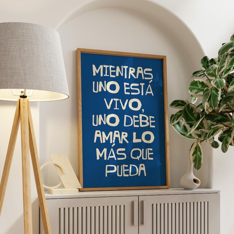 Może przedstawiać: Biały ceramiczny kubek z czarnym uchwytem i napisem "But First, Coffee" pogrubioną, czarną czcionką. Kubek jest ustawiony na rozmytym tle, sugerującym przytulne otoczenie.