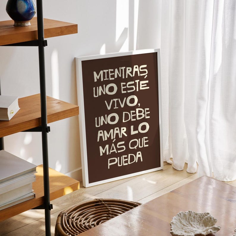 K&ouml;nnte beinhalten: Ein gerahmter Druck mit dem spanischen Text "Mientras uno este vivo, uno debe amar lo m&aacute;s que pueda" in Wei&szlig; auf braunem Hintergrund. Der Rahmen ist wei&szlig;, und der Druck lehnt an einer Wand.