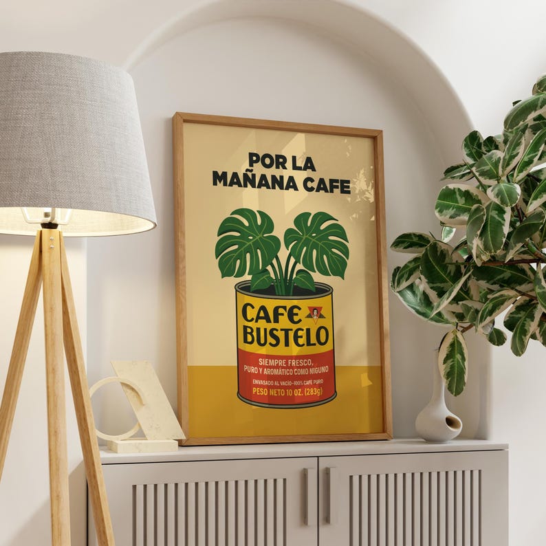 May include: A framed poster with a vintage design. The poster features the text "POR LA MA&Ntilde;ANA CAFE" at the top, with a graphic of a plant in a coffee can below. The can reads "CAFE BUSTELO" and "PESO NETO 10 OZ. (283g)".