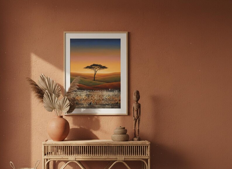 African savanna sunset art print in a white frame displayed above a boho entryway console table. The print shows a lone acacia tree silhouetted against a golden orange sky with tribal pattern border at the bottom. Styled with clay pots and pampas grass