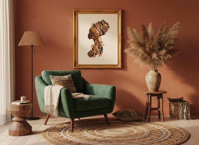 Elegant African queen portrait in a gold ornate frame on a warm terracotta wall. The art print shows a woman in profile with intricate tribal patterns and a decorative headwrap in brown, gold, and blue tones. Styled beside a teal green armchair with jute rug