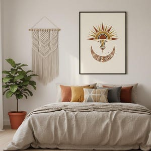 African tribal sun mask art print in black frame displayed above a boho bedroom bed with macrame wall hanging, earthy terracotta and cream tones, digital download wall decor