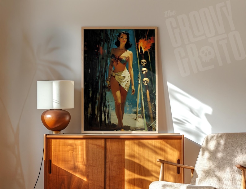 May include: A framed vintage-style print featuring a woman in a tropical setting. The artwork has a retro aesthetic with a color palette of blues, greens, and flesh tones. The print is displayed on a wooden cabinet with a lamp.