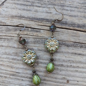 May include: A pair of dangle earrings with a floral design. The earrings feature a gold-colored metal with green and blue glass beads. The earrings have a hook closure and a teardrop-shaped bead at the bottom.