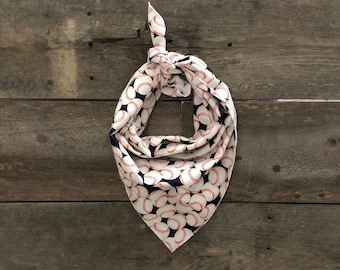 May include: A white and navy blue baseball-themed bandana with a repeating pattern of baseballs. The bandana is knotted at the top and hangs against a weathered wooden background.