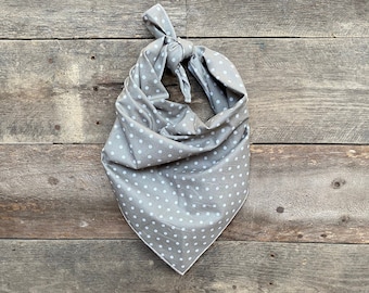 May include: A gray bandana with white polka dots, knotted at the top. The fabric is folded into a triangle shape. The background is a rustic wooden surface.