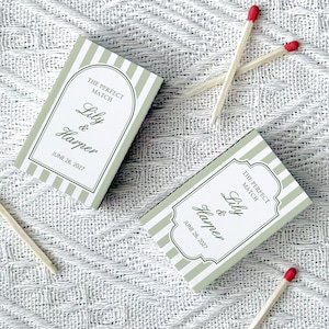May include: Two matchbox favors with green and white stripes, featuring the text "The Perfect Match" and names "Lily & Harper" with a date. Several matches with red tips are scattered around the boxes, on a textured white surface.