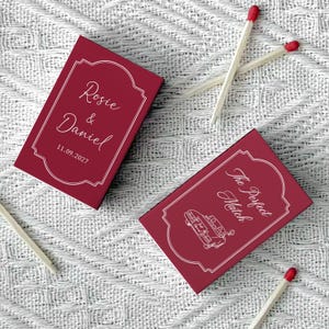 May include: Two burgundy matchboxes with white text and a decorative border. One box reads "Rosie & Daniel" and the date "11.09.2027". The other box says "The Perfect Match" with a car graphic.