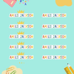 May include: A sheet of ten rectangular adhesive labels featuring the name AMELIE JACKSON in multicoloured letters. Five labels include a yellow crown icon above the name. The background is light blue with scattered paper clips and a ruler.