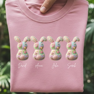 Może przedstawiać: Różowa koszulka z czterema aplikowanymi wzorami królików. Każdy królik ma wzór patchwork z kwiatowymi i kratkowanymi detalami. Pod spodem widnieją imiona "David", "Anna", "John" i "Sarah".