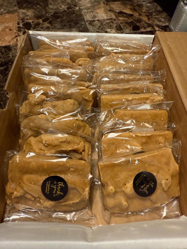 Peut inclure: Une bo&icirc;te en carton remplie de morceaux de fudge brun clair emball&eacute;s individuellement. Chaque morceau est scell&eacute; dans du plastique transparent. Certains morceaux ont un autocollant "Merci pour votre soutien".