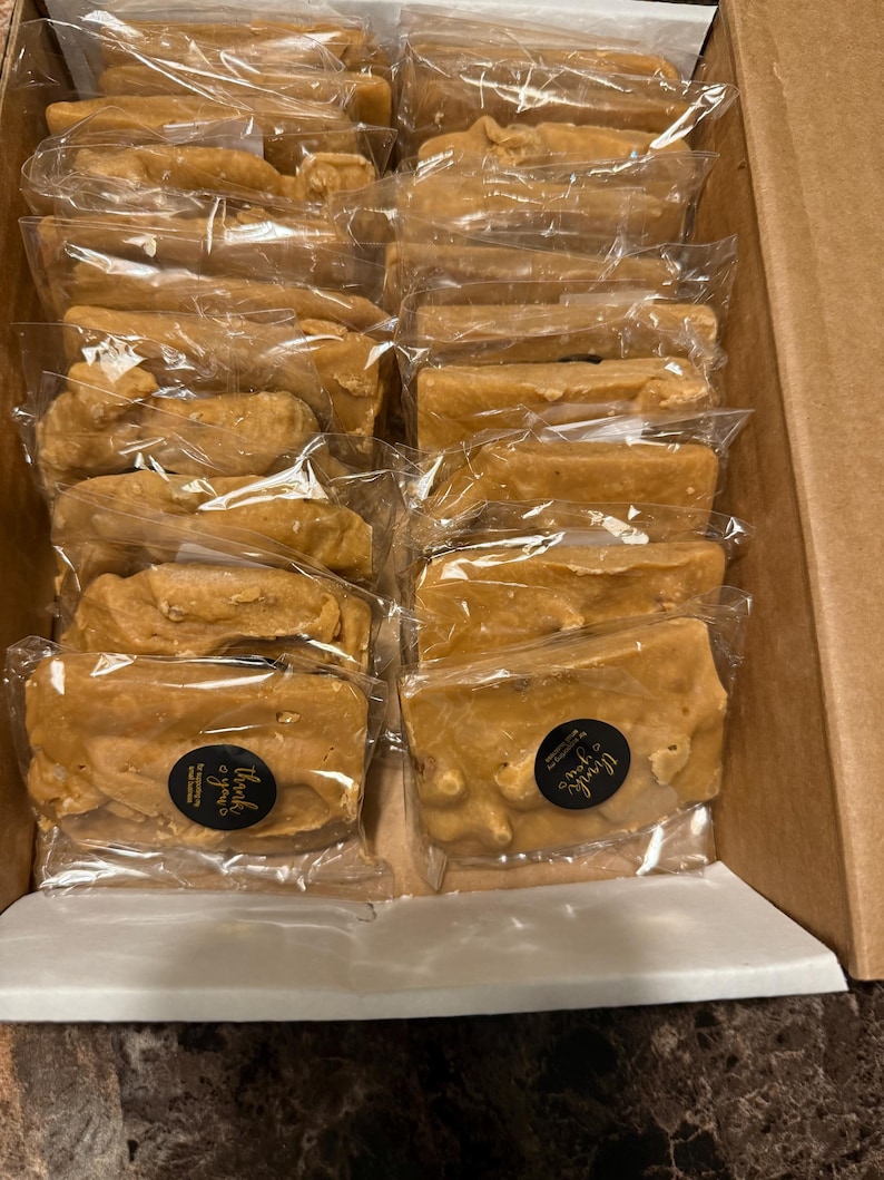 Peut inclure: Une bo&icirc;te en carton remplie de morceaux de fudge brun clair, emball&eacute;s individuellement. Chaque morceau est scell&eacute; dans du plastique transparent. Certains paquets ont un petit autocollant rond avec l'inscription "Thank you".