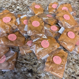 Peut inclure: Plusieurs morceaux de nougat aux noix emball&eacute;s individuellement dans des sachets en plastique transparent. Chaque sachet est scell&eacute; avec un autocollant rose portant l'inscription "thank you" en cursive. Le nougat a un aspect brun clair et brillant.