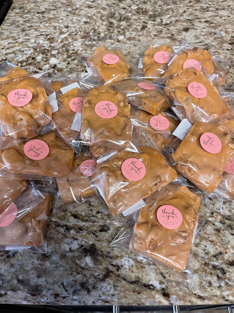 Peut inclure: Plusieurs morceaux de nougat aux noix emball&eacute;s individuellement dans des sachets en plastique transparent. Chaque sachet est scell&eacute; avec un autocollant rose portant l'inscription "thank you" en cursive. Le nougat a un aspect brun clair et brillant.