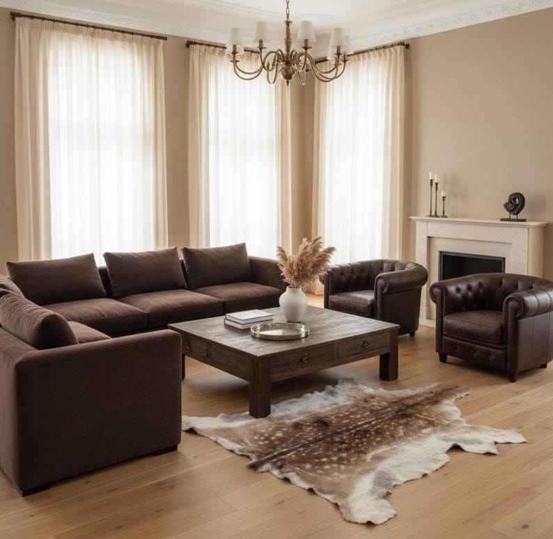 May include: A living room with brown furniture, including a sectional sofa, two armchairs, and a wooden coffee table. A decorative rug lies on the hardwood floor. The room has large windows with sheer curtains and a fireplace.