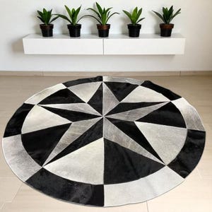 May include: A round rug with a geometric starburst design in black, white, and gray. The rug is made of a textured material and has a circular shape. The rug's diameter is approximately 60 inches.
