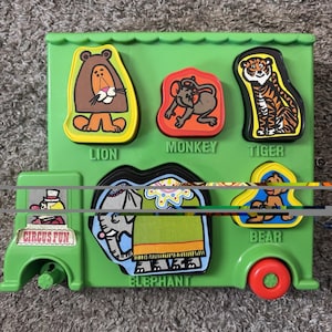 May include: A green plastic toy shaped like a bus with animal-shaped puzzle pieces. The puzzle pieces include a lion, monkey, tiger, bear, and elephant. The text "Circus Fun" is visible on the side of the bus.