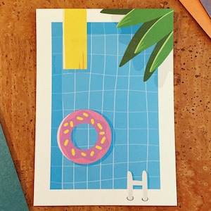 Könnte beinhalten: Eine Postkarte mit einem blauen Swimmingpool mit einem aufblasbaren Ring in Form eines rosa Donuts. Ein gelbes Handtuch hängt an der Seite, und grüne Palmenblätter sind zu sehen. Eine weiße Leiter befindet sich am Boden. Die Postkarte liegt auf einer braunen Korkoberfläche.
