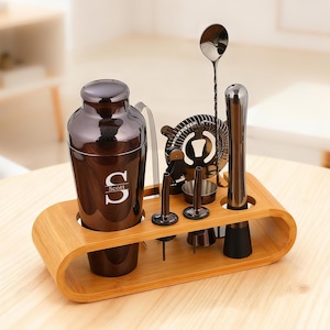 Pode incluir: Um conjunto completo de coqueteleira com acabamento metálico castanho, incluindo uma coqueteleira com o nome "Scott", um coador, uma colher, um pilão e jiggers. O conjunto é exibido numa bandeja de bambu.
