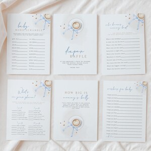 May include: Six white rectangular baby shower game cards featuring blue ribbon and coffee cup illustrations. The cards include titles like Baby Word Scramble, Diaper Raffle, Who Knows Mommy Best, What's On Your Phone, How Big Is Mommy's Belly, and Wishes For Baby.
