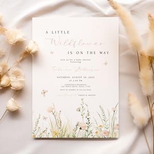 May include: A baby shower invitation with the text "A Little Wildflower Is On The Way." The invitation features a floral design with butterflies and is surrounded by dried flowers. The date and time are included.