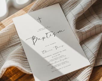 May include: A baptism invitation card with a cross symbol at the top. The card features elegant script text that reads "Baptism" and details for the event, including the daughter's name, date, time, and location. The card is set on a neutral-toned fabric.
