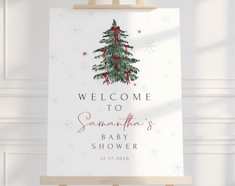 May include: A white sign on a wooden easel featuring a Christmas tree illustration with red bows. The sign says "Welcome to Samantha's Baby Shower" and the date 12.17.2026. Snowflake designs are scattered around the text and tree.