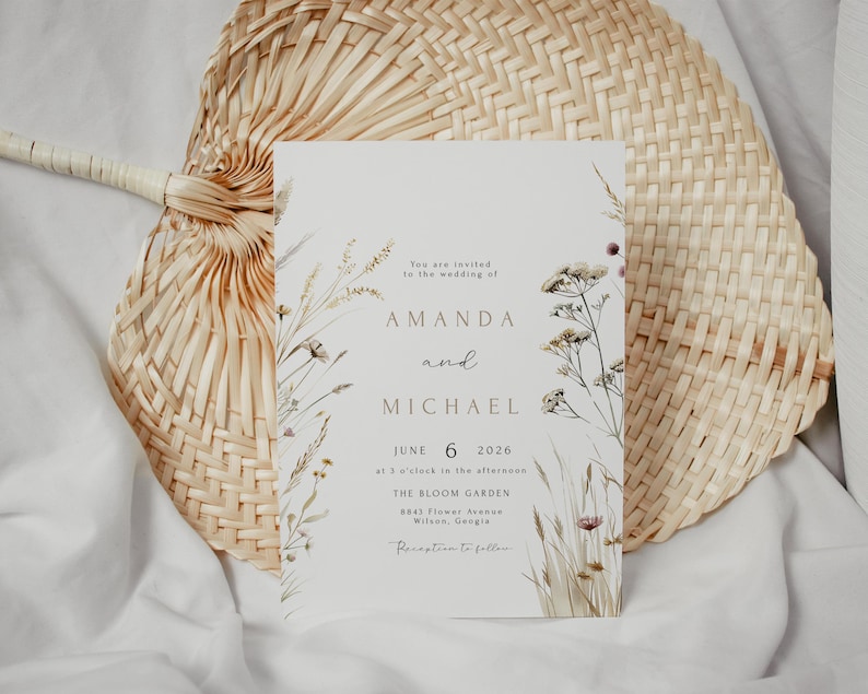 May include: A wedding invitation with floral illustrations and the names Amanda and Michael. The invitation is on a light background with text that reads "June 6 2026" and "The Bloom Garden". The invitation is placed on a woven fan.