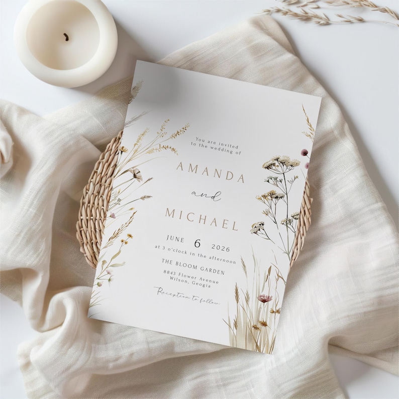 May include: A wedding invitation with the names "AMANDA" and "MICHAEL" in gold lettering, surrounded by floral illustrations. The invitation includes the date "JUNE 6 2026" and the venue "THE BLOOM GARDEN". A white candle and a woven basket are also visible.