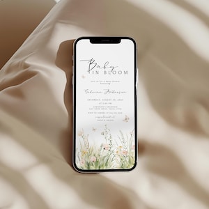 May include: A smartphone displays a baby shower invitation. The invitation features the text "Baby in Bloom" in elegant script, along with event details, including the date, time, and location. Delicate floral and butterfly illustrations adorn the bottom of the invitation.