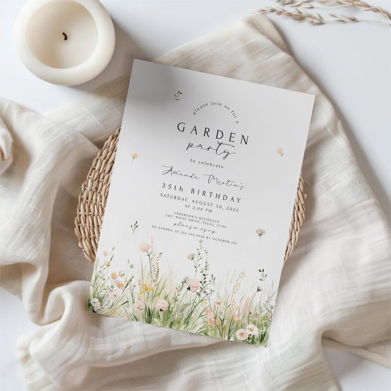 May include: A white invitation card with the text "GARDEN party" and "35th BIRTHDAY" in black. The card features a floral design at the bottom and is placed on a beige cloth with a woven basket and a white candle.