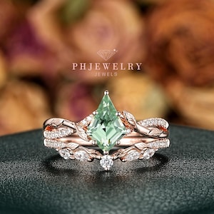 May include: A rose gold engagement ring set with a light green, kite-shaped center stone. The band features leaf and vine detailing, with smaller white stones. The ring set is displayed on a dark green surface, with the text "PHJEWELRY JEWELS".