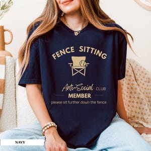 May include: Navy blue t-shirt with the text "FENCE SITTING Anti-Social CLUB MEMBER" and a graphic of a chair and baseball. The shirt also includes the phrase "please sit further down the fence."