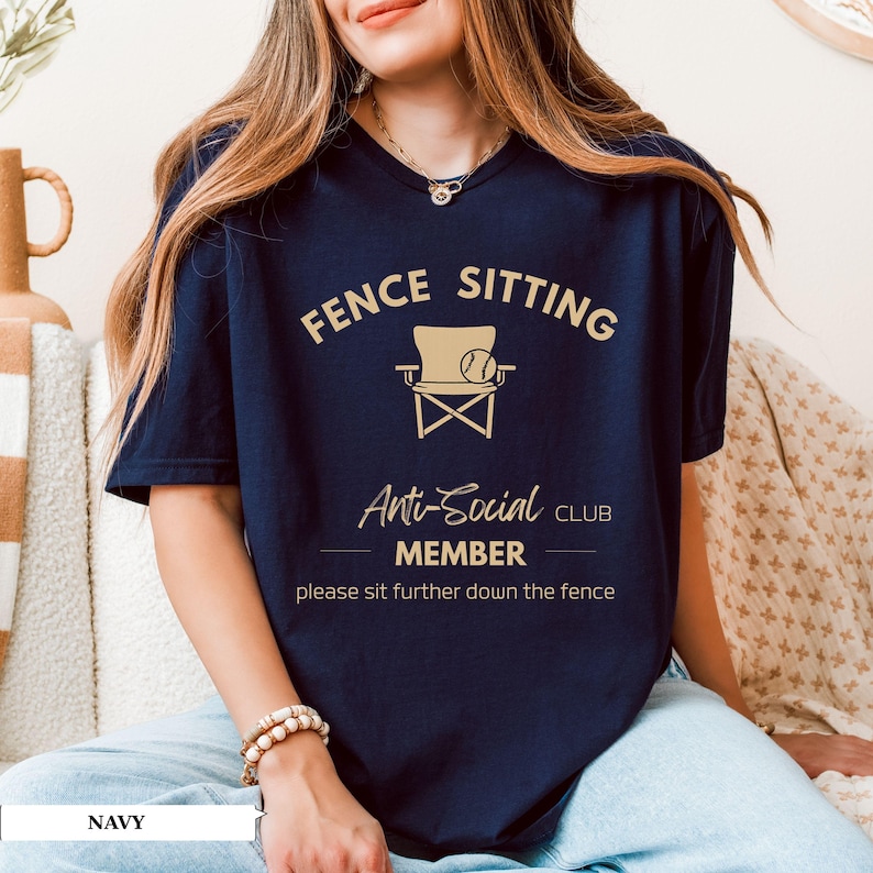 May include: Navy blue t-shirt with the text "FENCE SITTING Anti-Social CLUB MEMBER" and a graphic of a chair and baseball. The shirt also includes the phrase "please sit further down the fence."