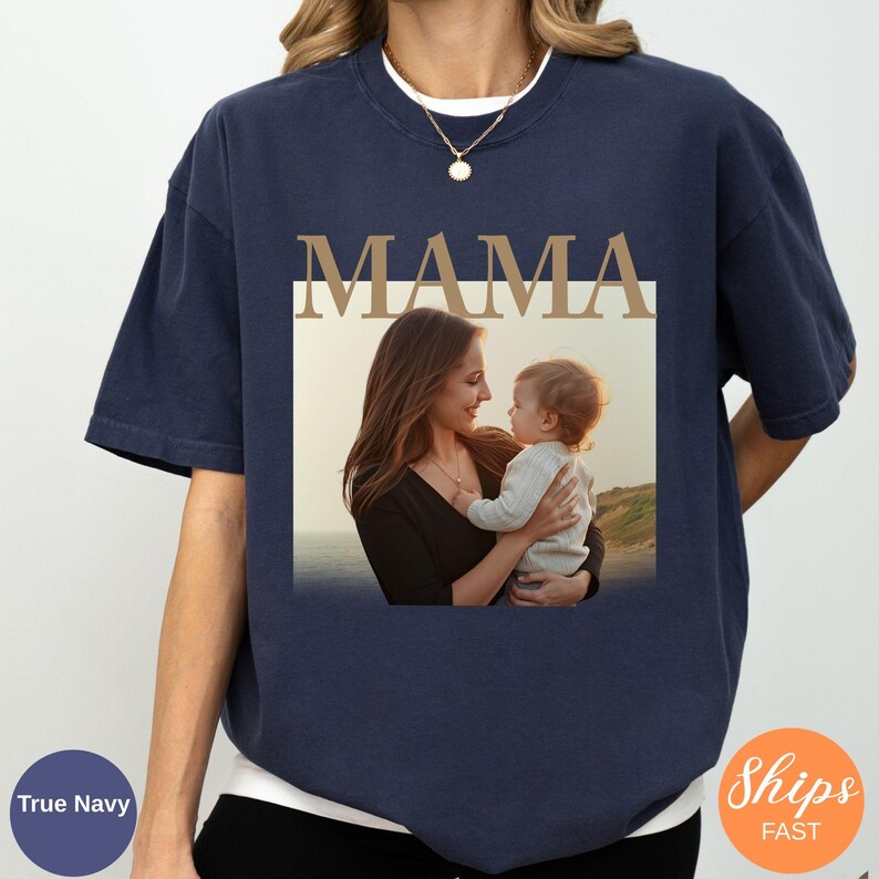May include: Navy blue t-shirt with the word "MAMA" in a gold font above a photo of a mother and child. The photo is in a white rectangle. The shirt is a relaxed fit.
