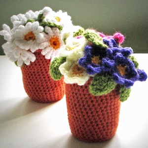 Könnte beinhalten: Zwei gehäkelte Blumentöpfe, einer mit weißen Gänseblümchen und der andere mit lila und weißen Blumen. Die Töpfe sind rotbraun.