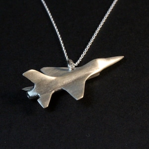 Op de afbeelding: Een zilveren ketting met een hanger in de vorm van een straaljager.