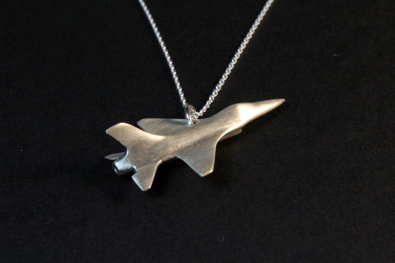 Op de afbeelding: Een zilveren ketting met een hanger in de vorm van een straaljager.