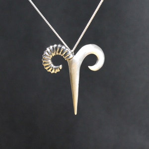 May include: A silver pendant necklace featuring a stylized ram's head design. The pendant has a detailed, curled horn and a smooth, pointed horn.