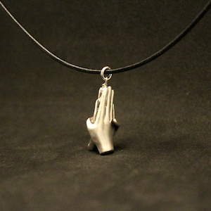 May include: A silver necklace with a pendant shaped like two hands clasped in prayer. The necklace is on a black leather cord.